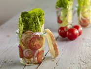 Romaine lettuce with red onion and tomatoes in glasses over wooden surface — Stock Photo
