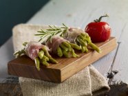 Green beans wrapped in bacon with rosemary on a small wooden board — Stock Photo