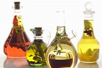Verschiedene Olivenöle mit Kräutern und Gewürzen auf weißem Hintergrund — Stockfoto
