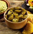 Jalapeos sottaceto, guacamole e tortilla chips in ciotola marrone su superficie di legno — Foto stock