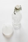 Vista close-up de uma garrafa de vidro e um funil em uma superfície branca — Fotografia de Stock