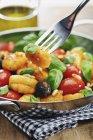 Ньокки с помидорами, оливками, кедровыми орехами и базиликом на плите с вилкой — стоковое фото