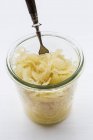 Sauerkraut en un vaso con un tenedor en la superficie blanca - foto de stock