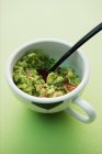Avocado dip in white cup over green surface — Stock Photo