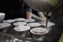 Closeup view of pouring chocolate mixture to aluminium moulds — Stock Photo