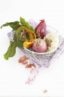 A trip of onions and yellow chard in a wird basket on a crocheted pot holder on white background — Stock Photo