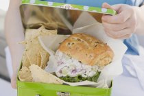 Крупним планом жінка тримає обідню коробку з курячим бутербродом і чіпсами — стокове фото