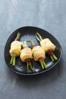 Rotoli di pasta sfoglia con asparagi e pancetta su piastra nera su superficie grigia — Foto stock