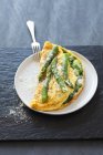 A spinach and asparagus omelette on white plate on black desk with fork — Stock Photo