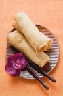Closeup top view of spring rolls with orchid and chopsticks on plate — Stock Photo