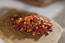 A pile of chilli flakes on a wooden plate — Stock Photo