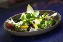 Змішаний свіжий салат у сірій тарілці на синій поверхні — стокове фото