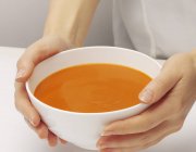 Manos sosteniendo un tazón de sopa de tomate - foto de stock
