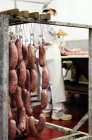 Salsicce italiane fresche appese in un macellaio con una persona sullo sfondo — Foto stock
