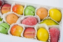 Vue rapprochée de bonbons à base de fruits de massepain jaune, vert, orange et rouge en boîte — Photo de stock