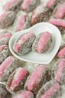 Close up of pink marzipan stuffed dates with two laying in a white heart shaped ceramic dish — Stock Photo