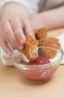 Vista de cerca de la mano del niño sumergiendo pepita de pollo en ketchup - foto de stock