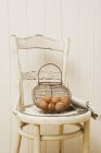 Vida morta com ovos em uma cesta de arame em uma cadeira antiquada — Fotografia de Stock