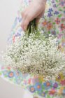 Cropped view of woman in flowery dress holding Gypsophila flowers — Stock Photo