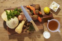 Ingredients for root vegetable soup on chopping board with knife over wooden surface — Stock Photo