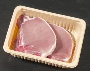 Chuletas de cerdo crudas en recipiente de plástico - foto de stock