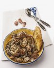 Sauteed clams with garlic and bread in yellow plate over table — Stock Photo