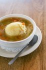 Vegetable broth with matzo dumpling in white bowl over plate with spoon — Stock Photo