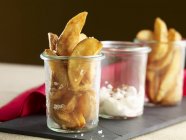 Potato wedges with a peppery dip in glass cups over black desk — Stock Photo