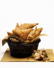 Closeup view of samosas with paper in basket and broken one beside — Stock Photo