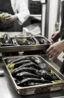 Обрізаний вид людей біля лотків баклажанів на комерційній кухні — стокове фото