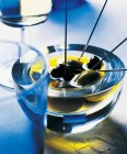 Aceitunas en aceite de oliva en un recipiente de vidrio sobre superficie azul - foto de stock
