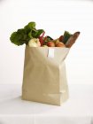 Свежие фрукты и овощи в бумажном пакете на белой поверхности — стоковое фото