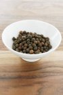 Closeup view of an allspice heap in a white bowl on a wooden surface — Stock Photo