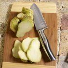 Galanga raiz, inteira e cortada, numa tábua de cortar com uma faca — Fotografia de Stock