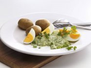 Франкфуртский зеленый соус с яйцами и картошкой на белой тарелке над деревянным столом — стоковое фото