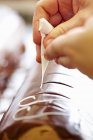 Close up vista recortada de mãos colocando glacê branco no esmalte de chocolate — Fotografia de Stock