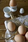 Vista close-up de ovos castanhos com palha em uma placa e em copos de ovo — Fotografia de Stock