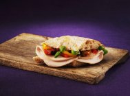Ein Truthahn-Braten-Paprika-Basilikum-Sandwich auf Holztisch vor violettem Hintergrund — Stockfoto