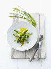 Green asparagus with olive oil and garlic chives for Easter on white plate over wooden surface with fork and knife — Stock Photo