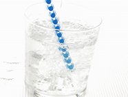 Closeup view of sparkling mineral water with ice cubes and straw in glass — Stock Photo