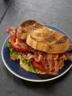 Крупним планом вигляд смаженого бекону, салату та бутерброду з помідорами на чорній тарілці — стокове фото