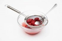 Closeup view of raspberries with sieve and spoon in bowl — Stock Photo