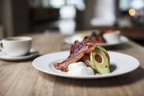 Nahaufnahme von Toast mit Speck, pochiertem Ei und Avocado auf weißem Teller über Holzoberfläche — Stockfoto