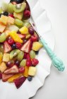 Vista de cerca de la ensalada de frutas de colores con cuchara en el plato - foto de stock