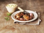Coq au vin with mashed potatoes  on white plate with fork over wooden surface — Stock Photo