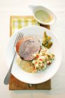 A sliced of turkey roulade with potato salad and gherkins  on white plate with fork — Stock Photo