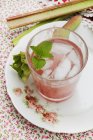 Nahaufnahme von Rhabarberschorle mit Eiswürfeln im Glas und Rhabarberstücken auf rosa gemustertem Teller — Stockfoto