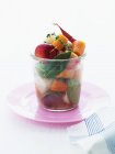 Un arrangement de légumes, pommes et herbes dans un verre sur une assiette rose — Photo de stock