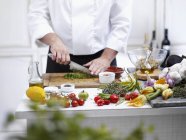 Chef cortando legumes com faca nas mãos sobre mesa de madeira, parte central — Fotografia de Stock