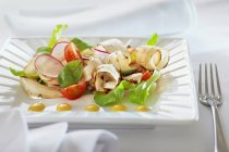 Черный салат с редькой и помидорами на белой тарелке — стоковое фото